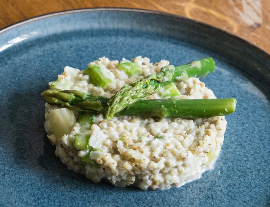 Sorghotto crémeux au parmesan, garni de morceaux et de pointes d’asperges vertes, présenté sur une assiette.