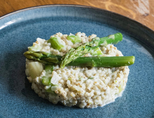 Sorghotto crémeux au parmesan, garni de morceaux et de pointes d’asperges vertes, présenté sur une assiette.